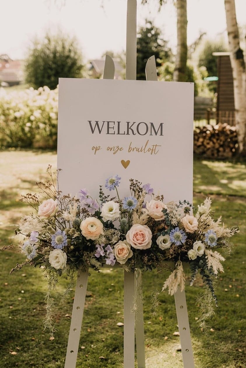 Bloemwerk op een welkomstbord voor de bruiloft, met rozen, ranonkels en eucalyptus in een tuin