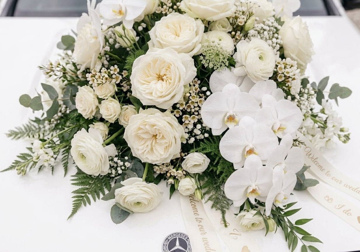 Wit bloemwerk met rozen en orchideeën op de motorkap van de witte trouwauto