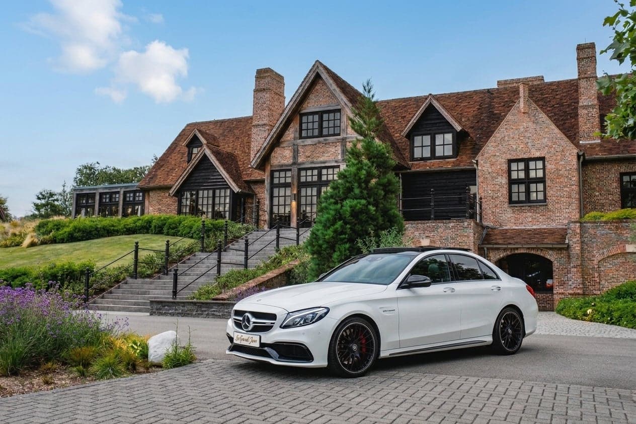 Witte Mercedes-AMG C63 S voor een landgoed onder een blauwe lucht